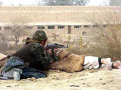 A Northern Alliance fighter seeks cover behind a corpse during battle at a fortress in Qala-i-Jangy. The last 150 Taliban holdouts there were killed, according to an Afghan security official.