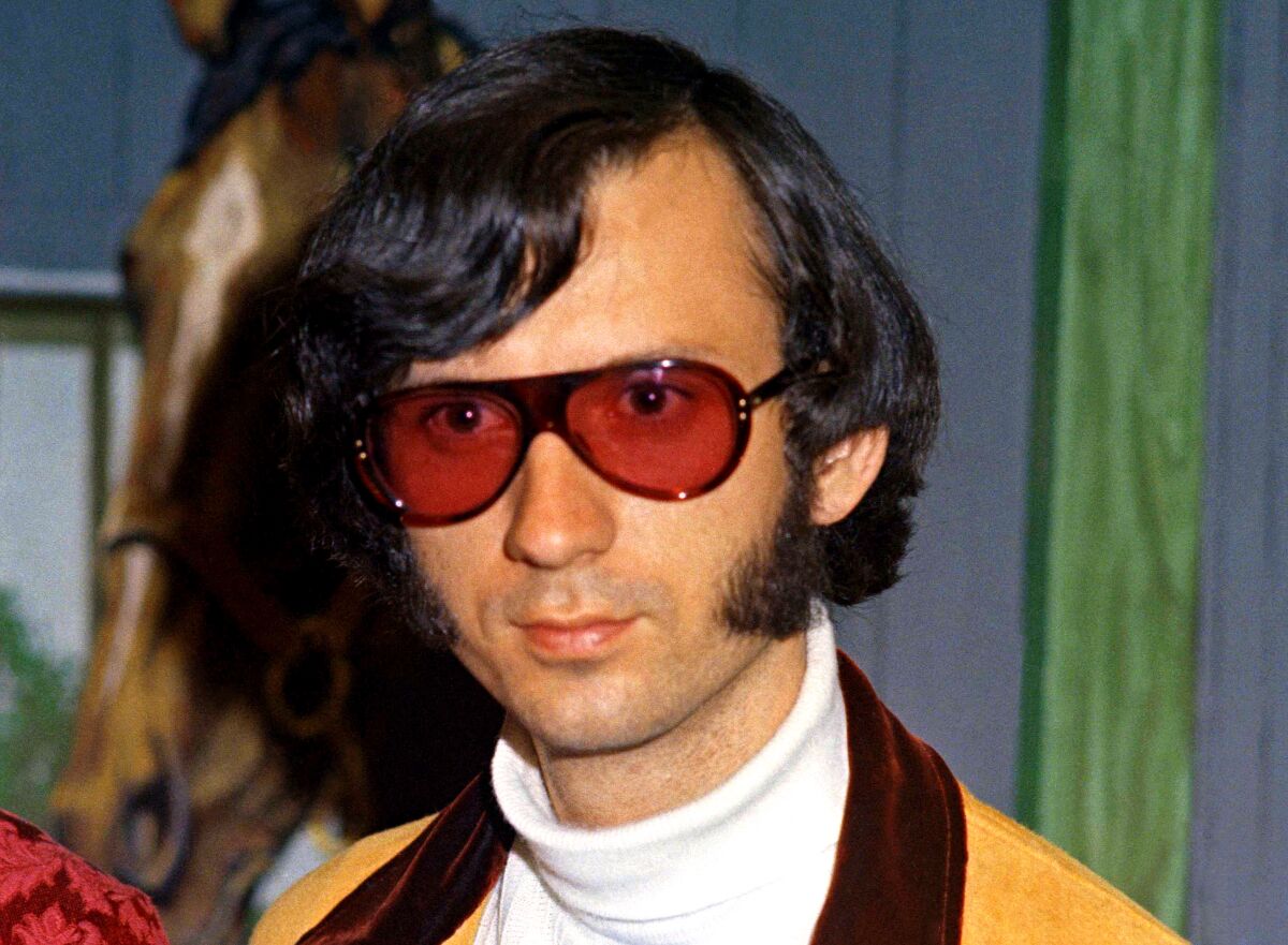 A man with bushy sideburns and red-tinted sunglasses, in the 1960s.