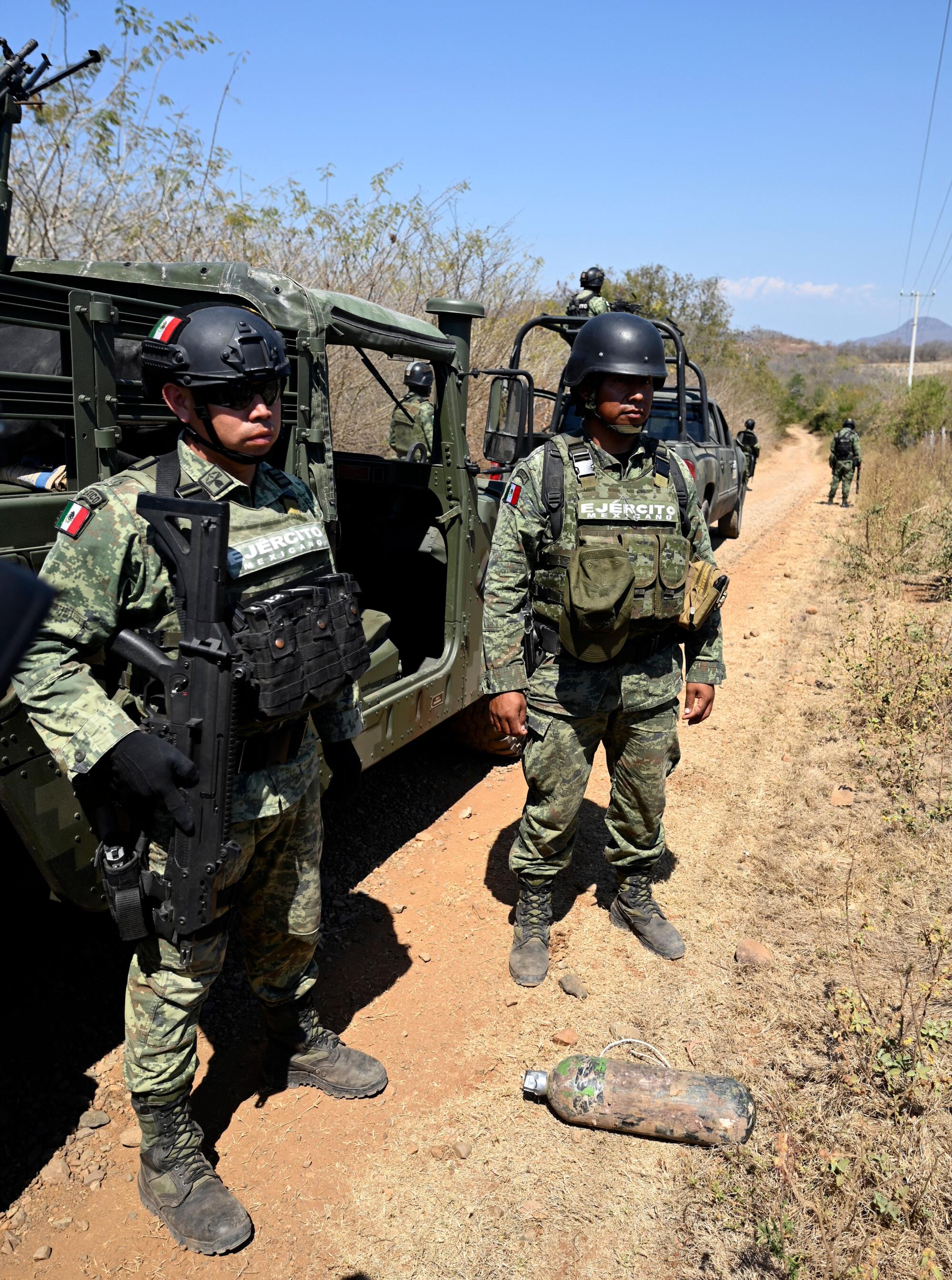 Soldiers of the special forces of the Mexican army show an explosive device on the side of a dirt road.