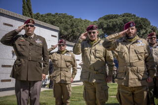 Active duty and retired U.S. Army paratroopers salute while standing in a group at a cemetery.