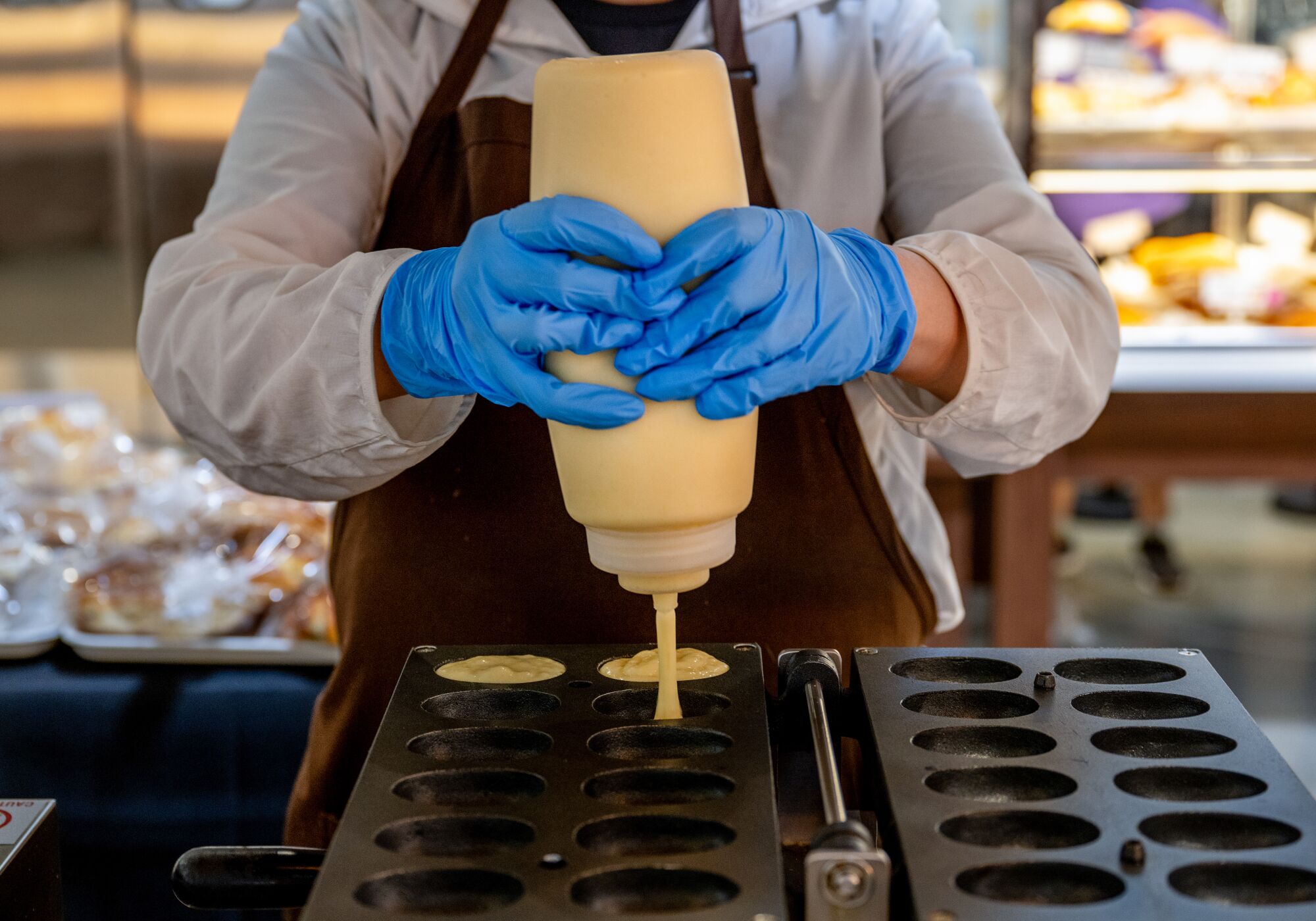 A cafe worker pours batter into small tins to make egg waffle cakes.