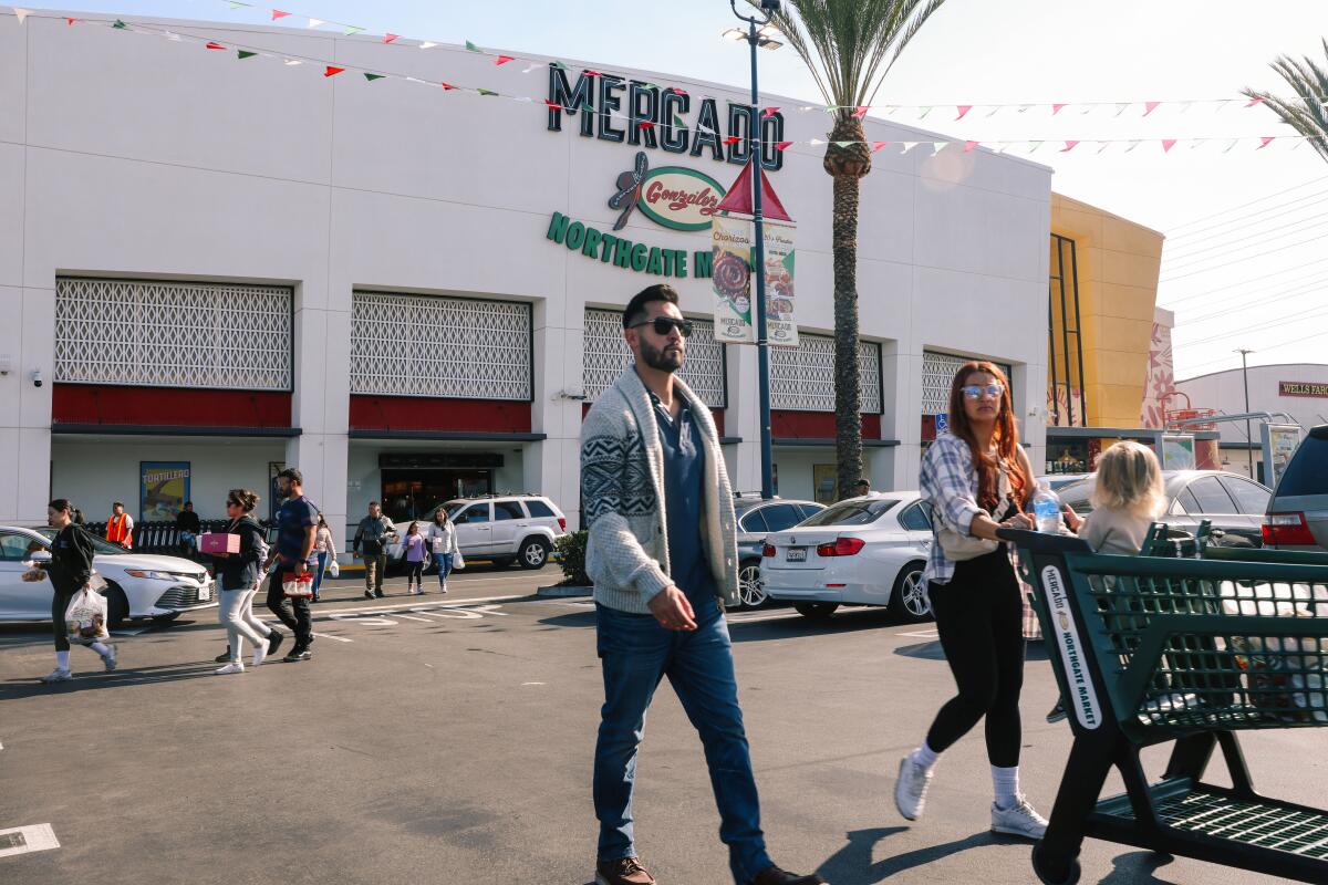An outdoor photo of people walking through a parking lot in front of the Mercado González Northgate Market.