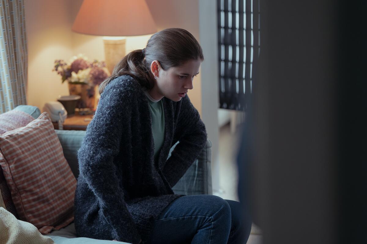 A young woman hunches over in pain on a sofa.