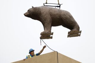 San Diego CA - May 22: Two California grizzly bear statues and flag poles were installed on the roof of the San Diego Automotive Museum in Balboa Park as part of a six-year, $715,000 preservation effort in keeping with the 1935 California Pacific International Exposition. Here Shane Liberty guides one of the bears as it is craned onto the roof on Monday, May 22, 2023. (K.C. Alfred / The San Diego Union-Tribune)