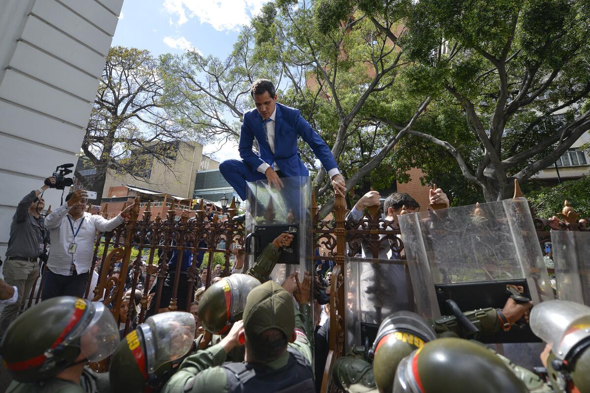 Venezuelan National Assembly President Juan Guaido tries to climb the fence to enter the legislative compound after he and other opposition lawmakers were blocked by police from attending a special session in Caracas on Jan. 5, 2020.