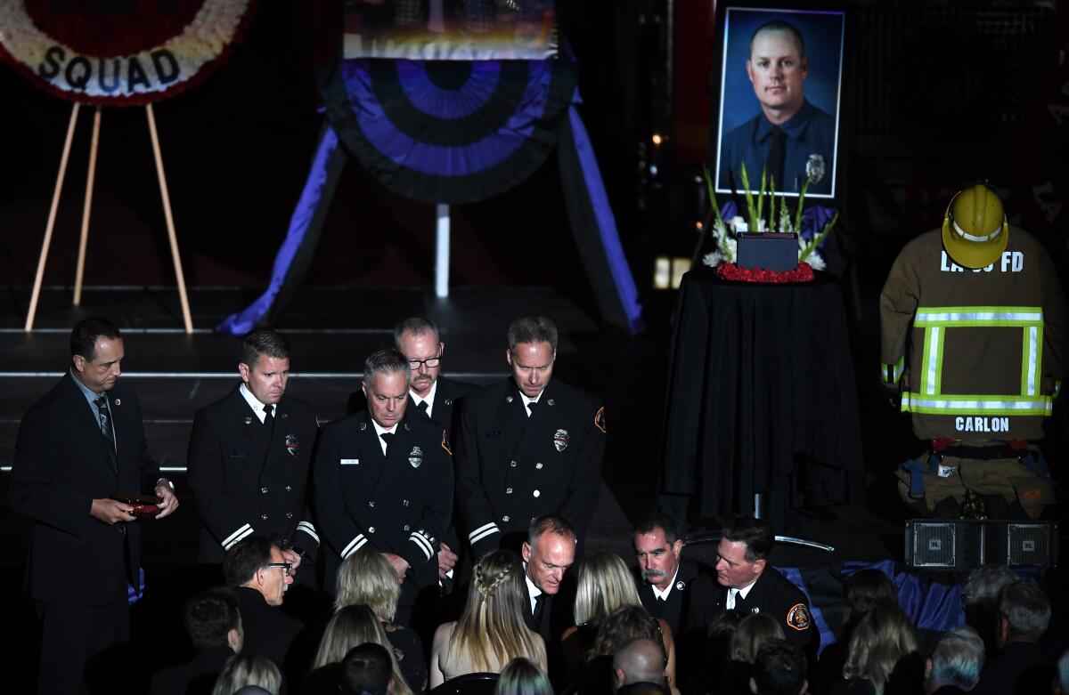 A photo of Tory Carlon is seen behind firefighters at a memorial