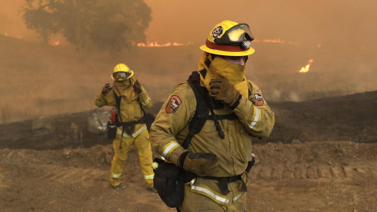 Firefighters with Cal Fire Mendocino Unit cover themselves from smoke and ash created by an advancing wildfire Monday, in Lakeport, Calif. A pair of wildfires that prompted evacuation orders for thousands of people are barreling toward small lake towns in Northern California.