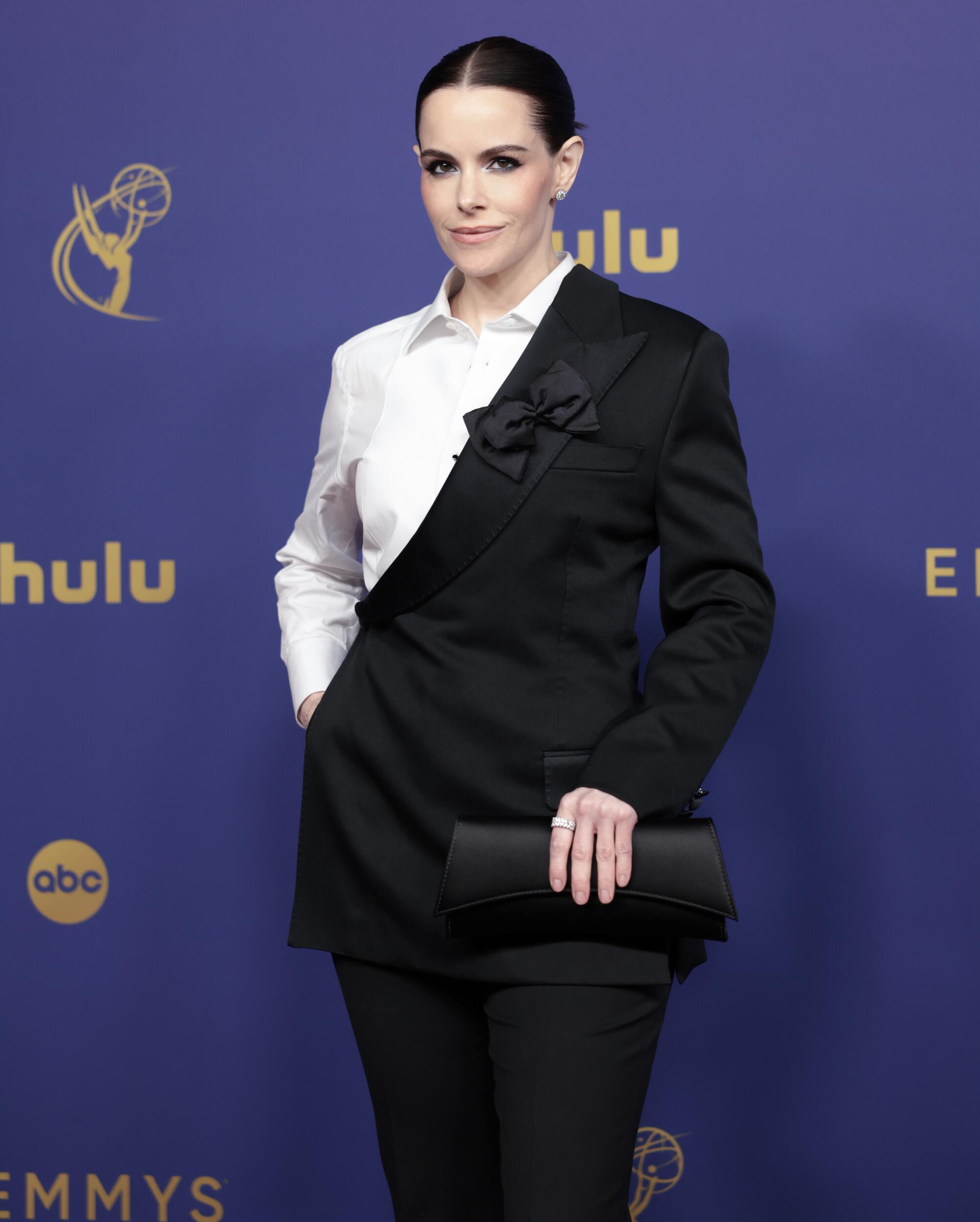 Emily Hampshire wears a white and black suit.