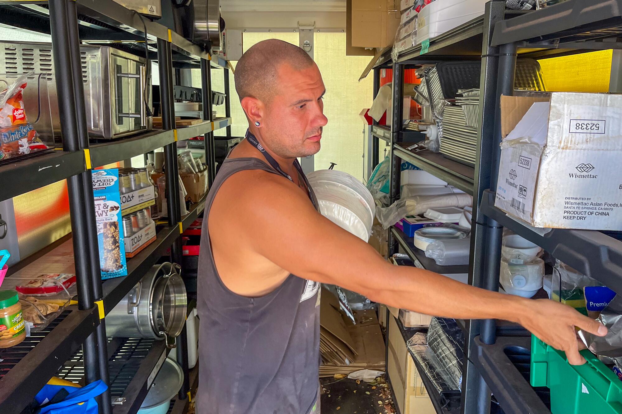 A man in a tank top among shelves filled with goods.