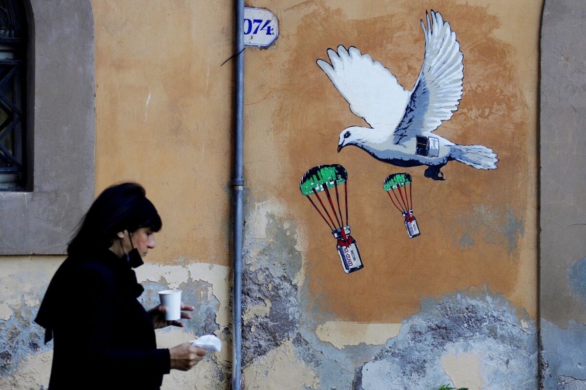 FILE - A woman walks past a mural depicting a white dove parachuting COVID-19 vaccine vials, posted near the Italian Health Ministry Headquarters in Rome, April 4, 2021. The pandemic is again roaring across parts of Western Europe, a prosperous region with relatively high vaccination rates and good health care systems but where lockdown measures to rein in the virus are largely a thing of the past. Italy, an early victim of the pandemic, has a high vaccination rate, but is also seeing numbers edge higher, which experts believe is due to vaccine efficacy wearing off. (AP Photo/Gregorio Borgia, file)