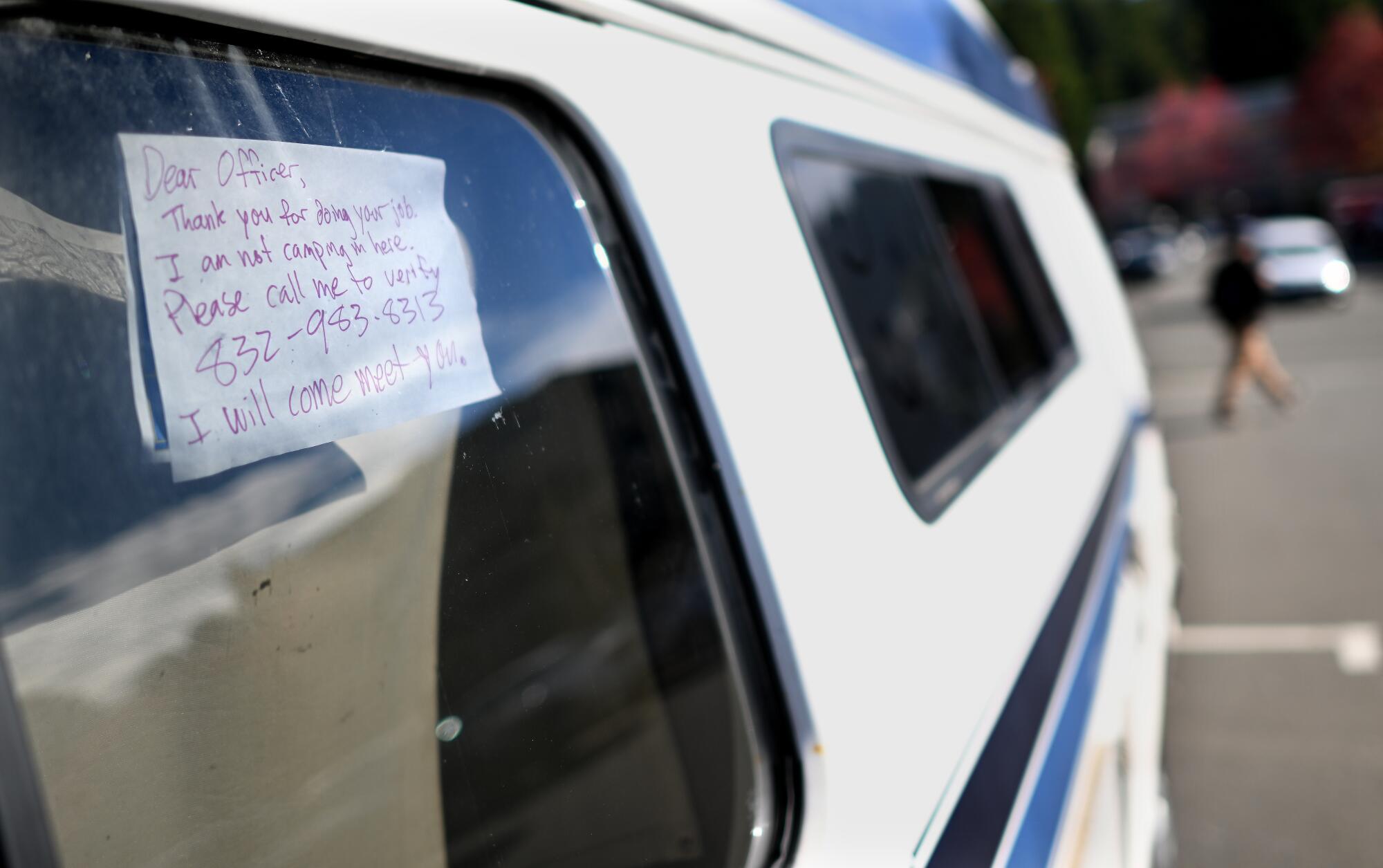 A handwritten note in red ink is taped on the inside of a car window.