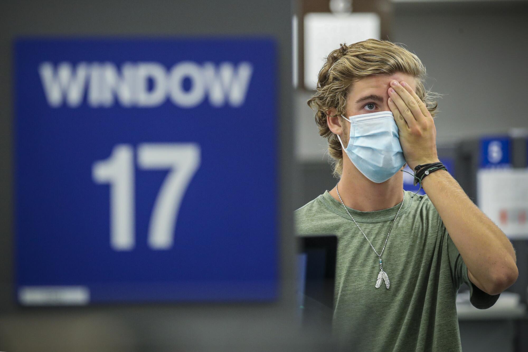 A teenager wearing a mask covers one eye with his hand while applying for his learner's permit at a DMV field office