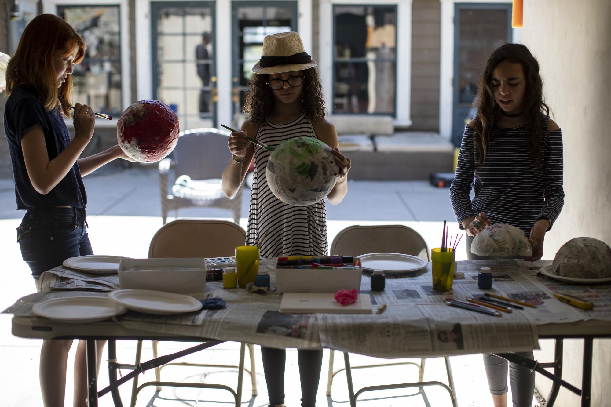 Kat Bristow, left, Carmen Furbush and Penelope Roth work on papier-mache masks in art class inside the Roths' garage.