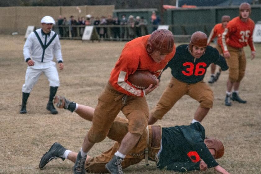 A young man in an old-time football uniform charges up the field while evading tacklers.