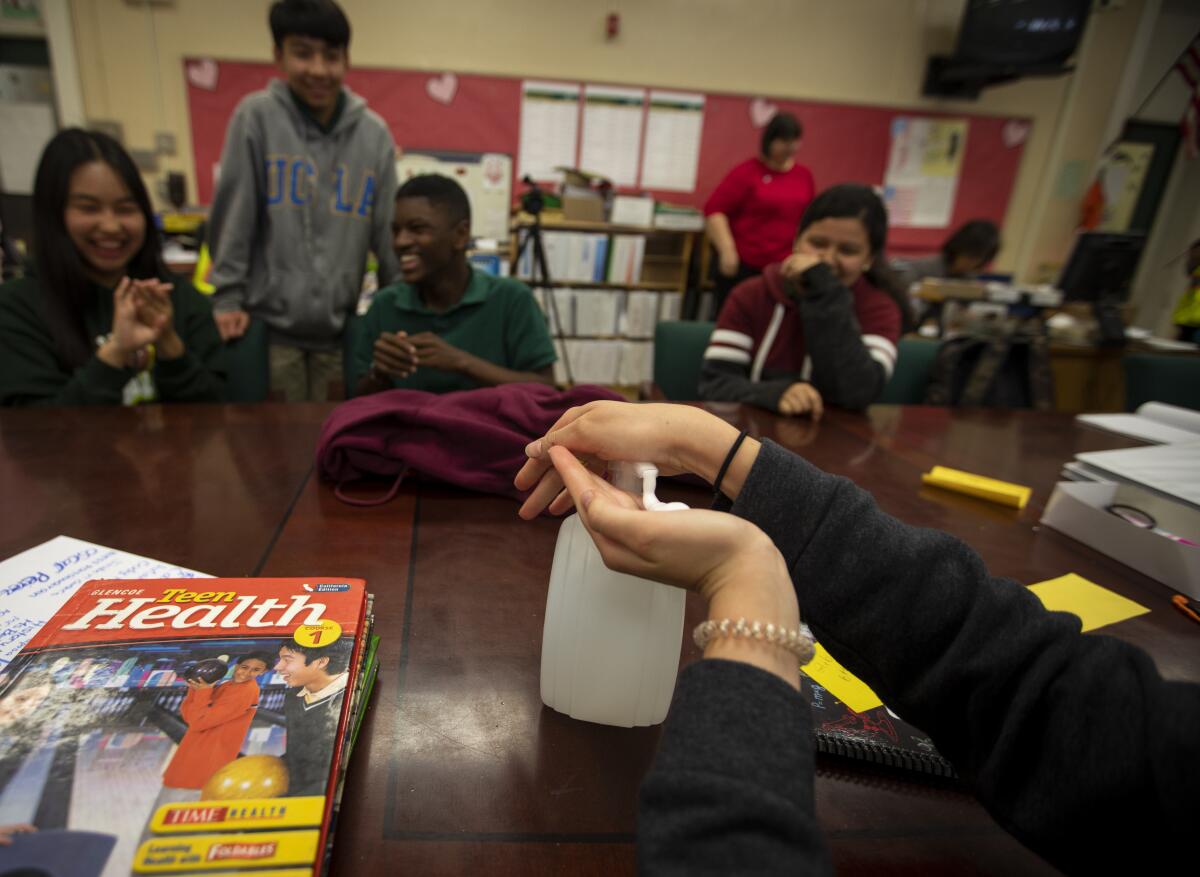 One student pumps sanitizer into her hand as her middle school classmates look on.