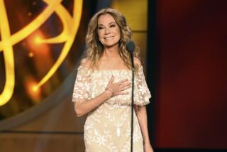 Kathie Lee Gifford smiles while holding her right hand to her heart onstage in a formal gown