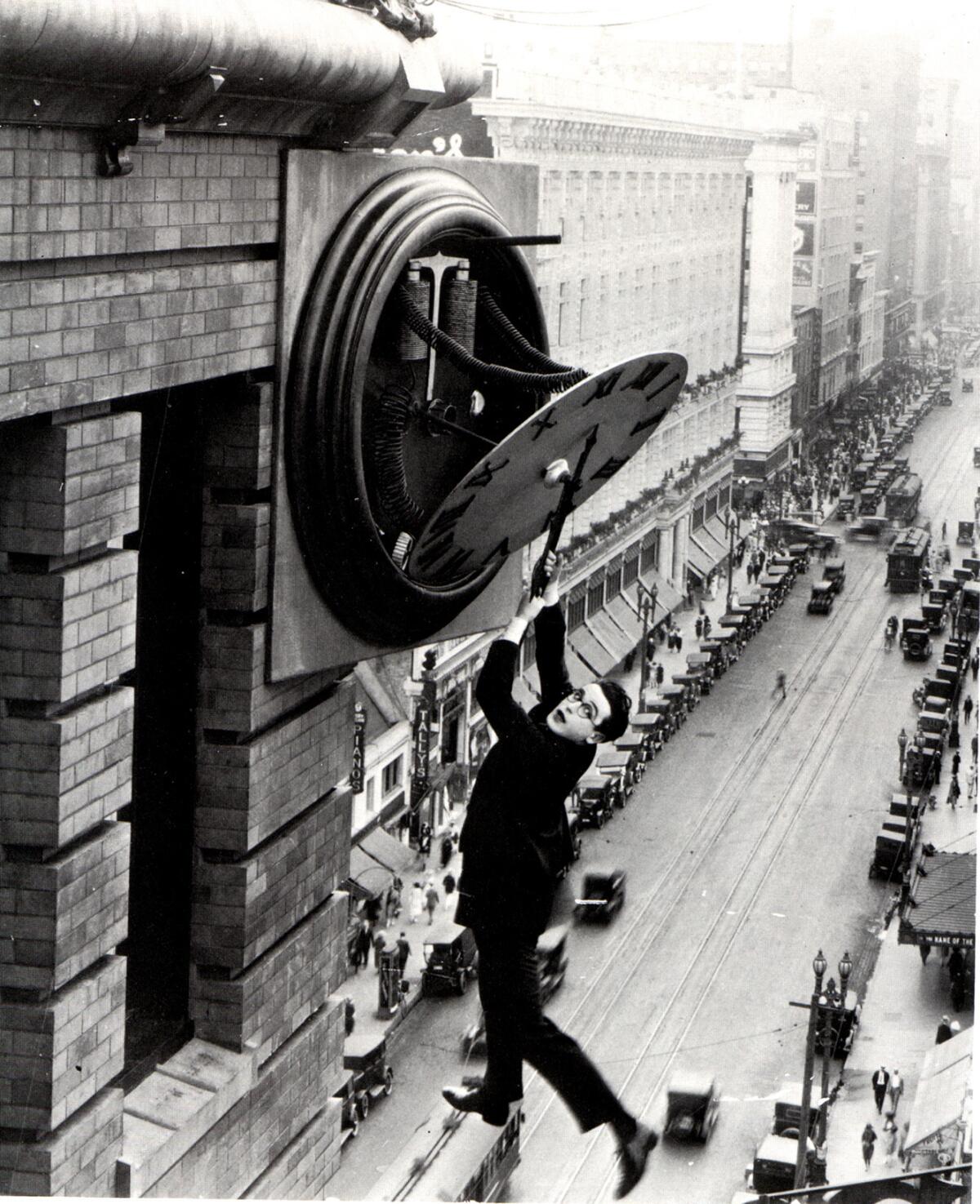 A man dangles from a clock face on the side of a building high above downtown L.A.