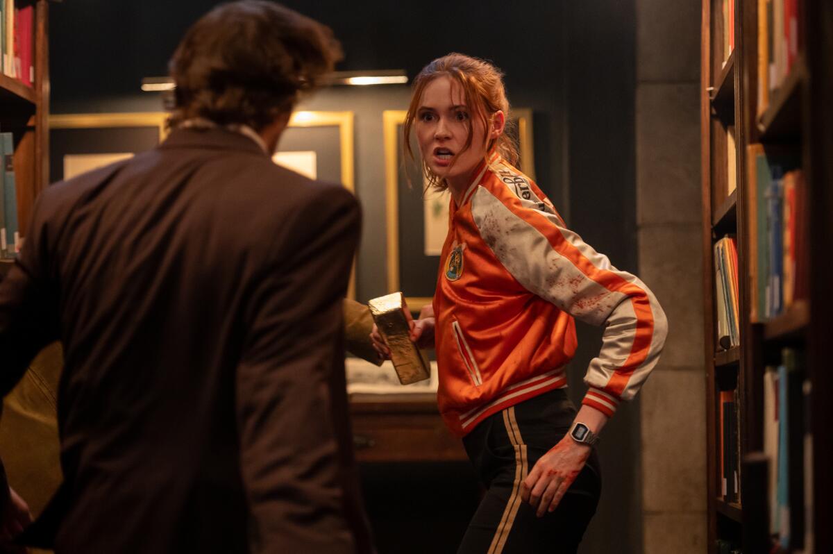 A woman holds a gold bar in a library looking defensive against a man approaching her