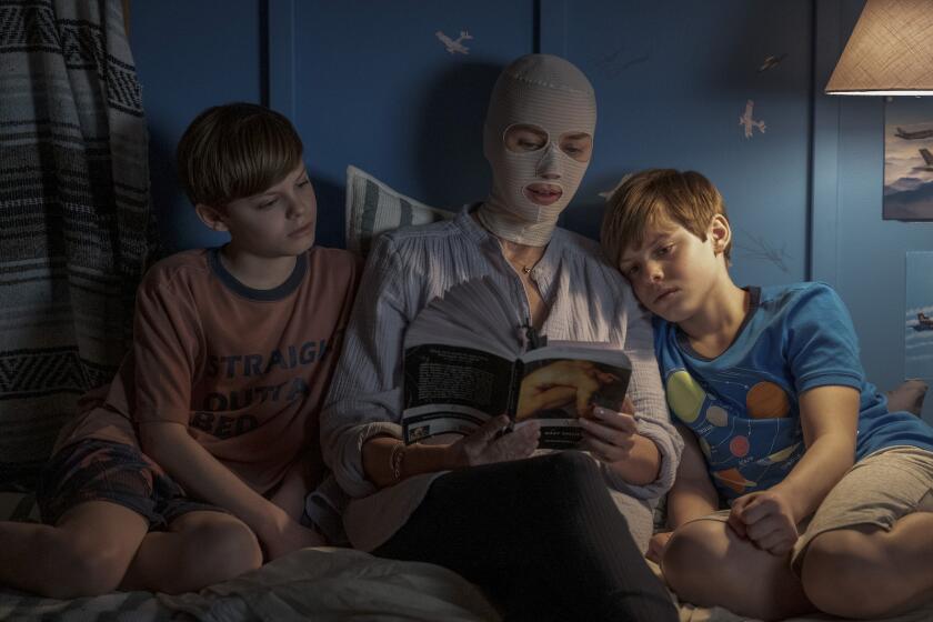 A woman with a bandaged face reads to two boys in the movie "Goodnight Mommy."