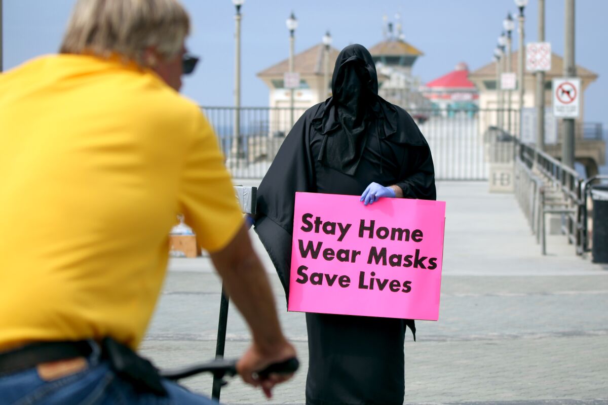 The Grim Reaper, also known as Spencer Kelly from Huntington Beach, holds a sign at Pier Plaza in Huntington Beach on Friday. The three-person protest was put on by Indivisible OC 48.