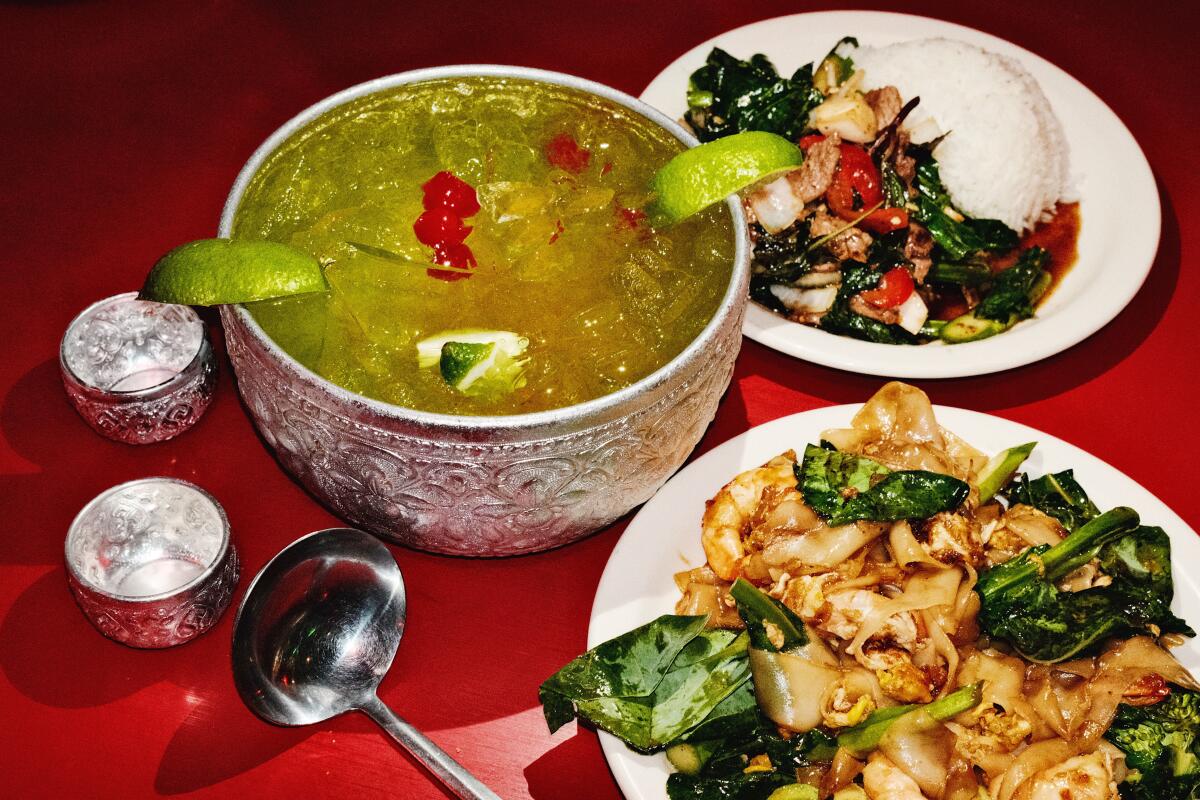 A bright green cocktail in a large-format silver bowl on a red table with ladle and stir-fries at Koreatown bar Thai Angel