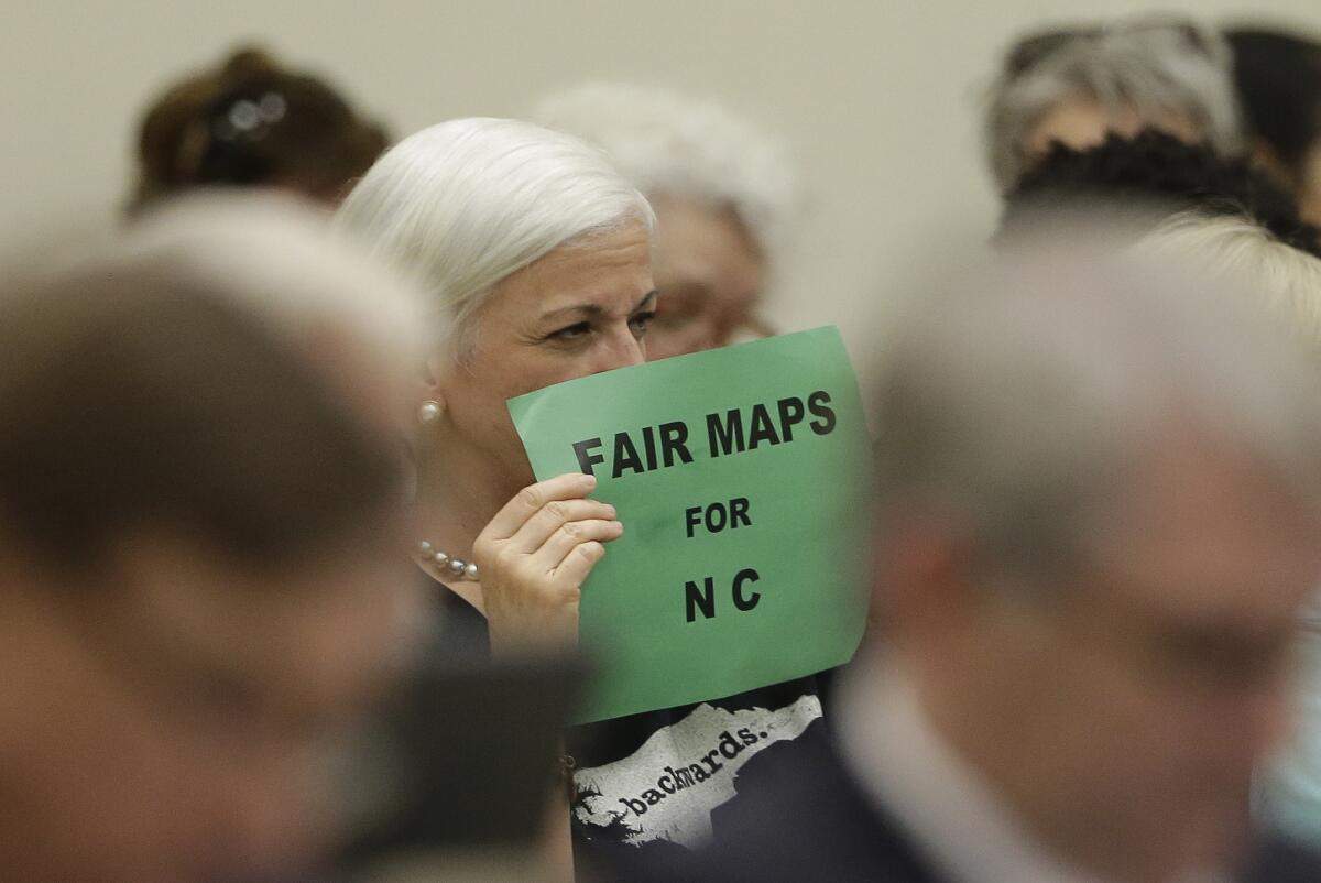 A member of the gallery tries to display her sign while lawmakers convene during a joint select committee meeting on redistricting in Raleigh, N.C., July 26, 2017.