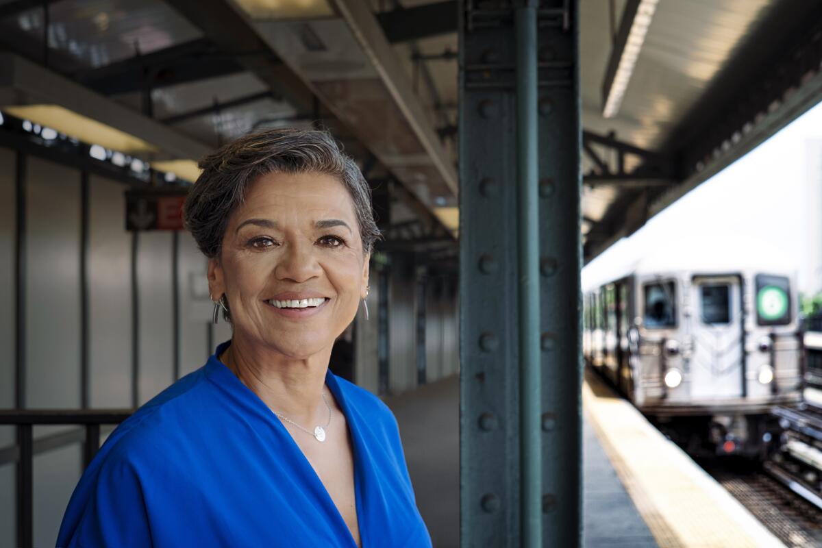 Sonia Manzano, in a blue top, stands on a subway platform as a train approaches.