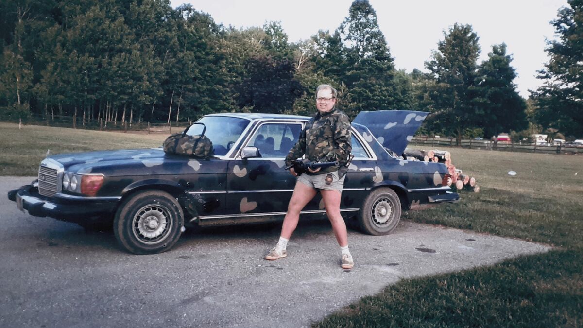 A man brandishing a rifle in front of a camouflage-painted Mercedes-Benz in the documentary "2nd Chance."