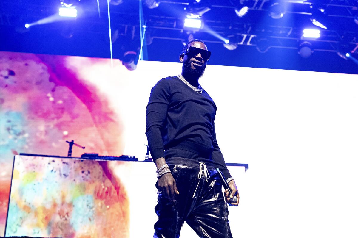 Gucci Mane wears a black shirt and pants as he stands on stage during a concert performance