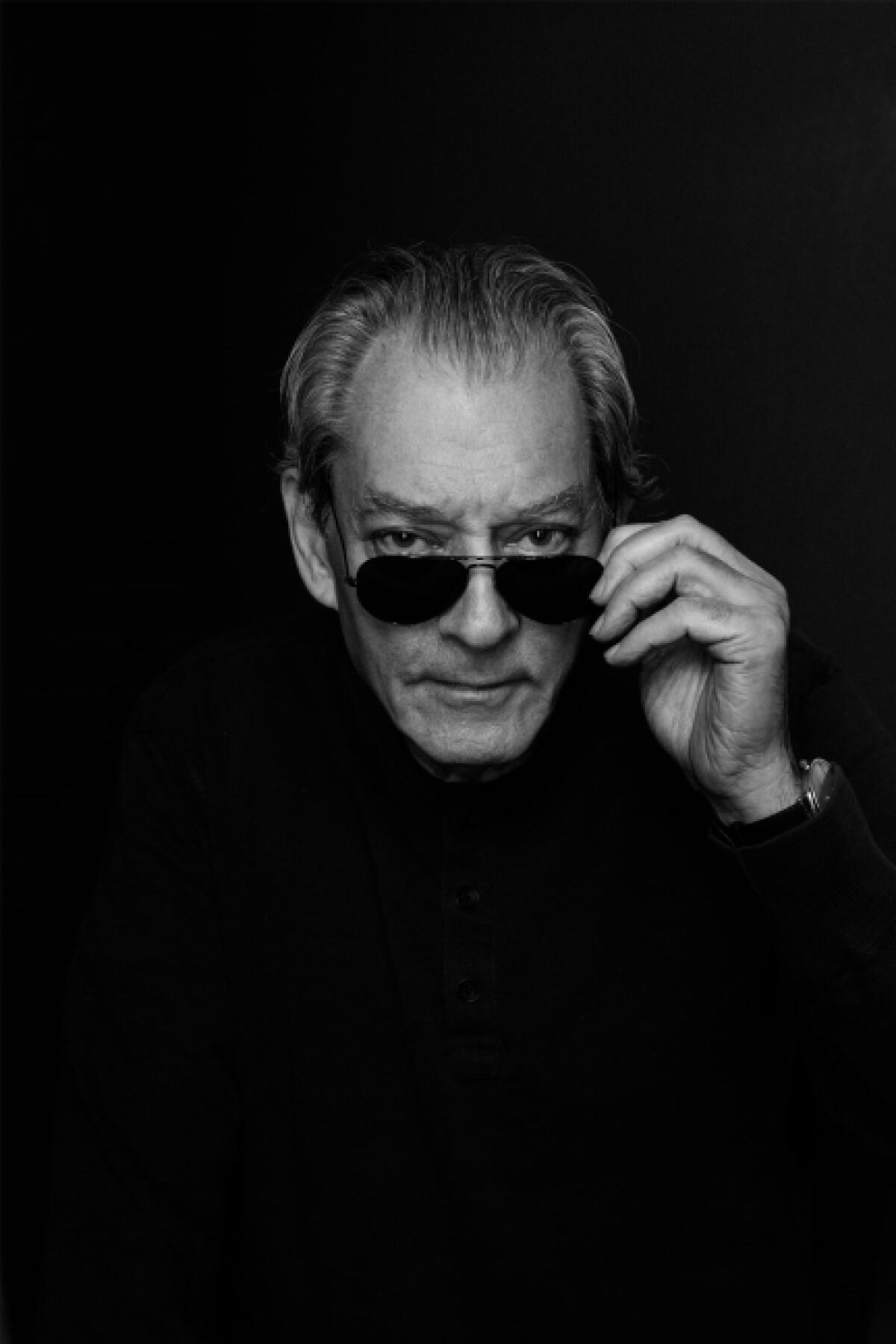 Paul Auster tilts his dark sunglasses down to show his eyes in a monochromatic portrait