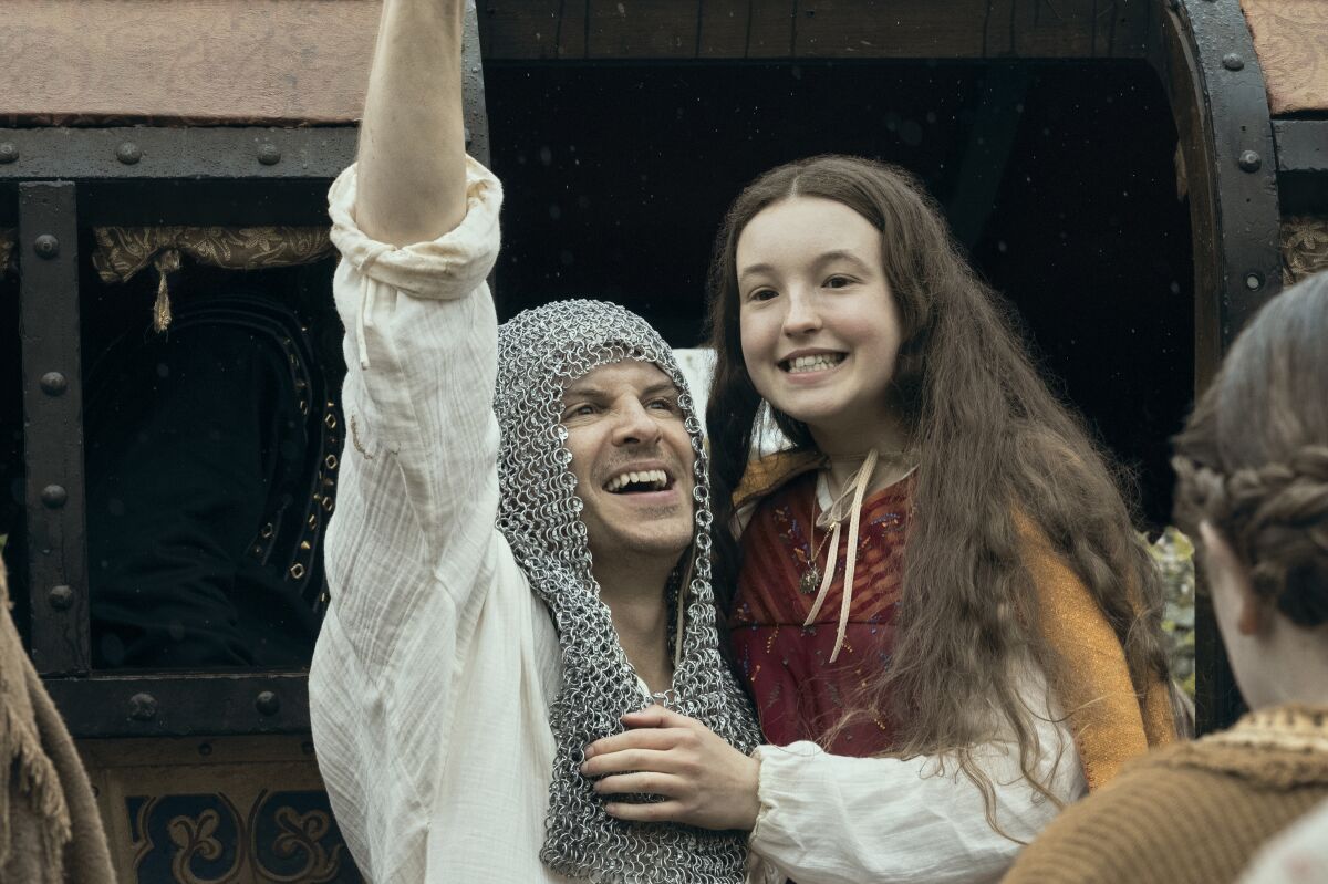 A man in chain-mail head covering and a young girl in homespun clothing smile triumphantly.