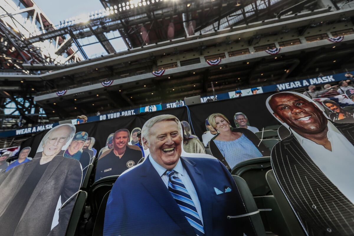 Cutouts of Vin Scully and Magic Johnson stand behind the Dodgers' dugout at Globe Life Field in Arlington, Texas.