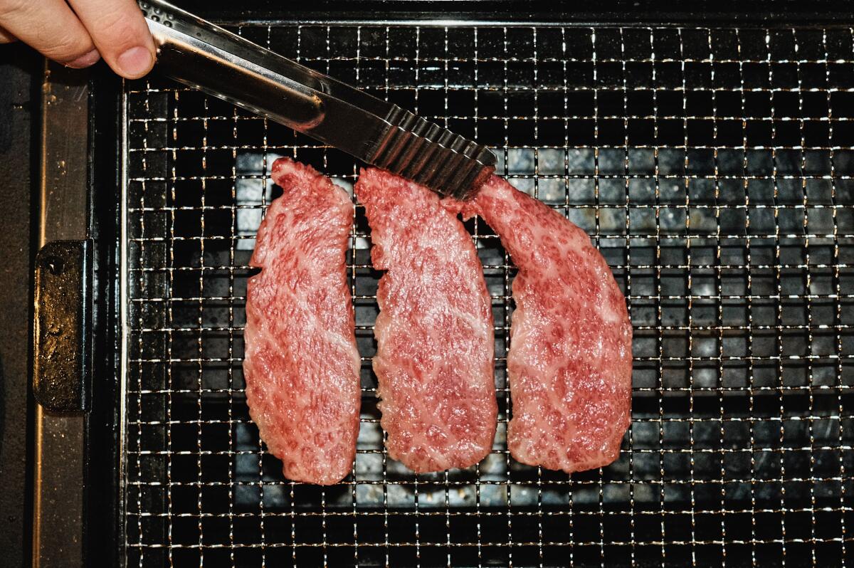 Three pieces of Wagyu steak and metal tongs on a grill at Moohan Korean BBQ in Koreatown.