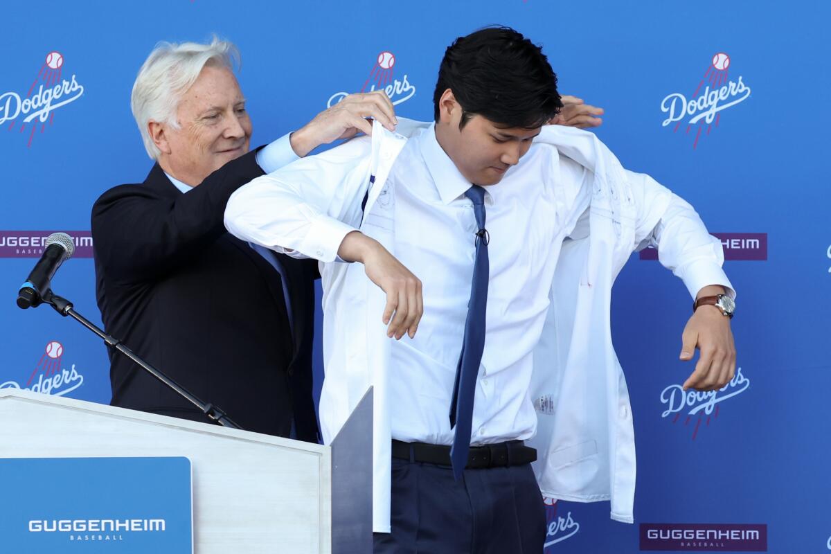 Dodgers owner Mark Walter helps Shohei Ohtani put on a jersey during a news conference on Dec. 14, 2023, at Dodger Stadium.
