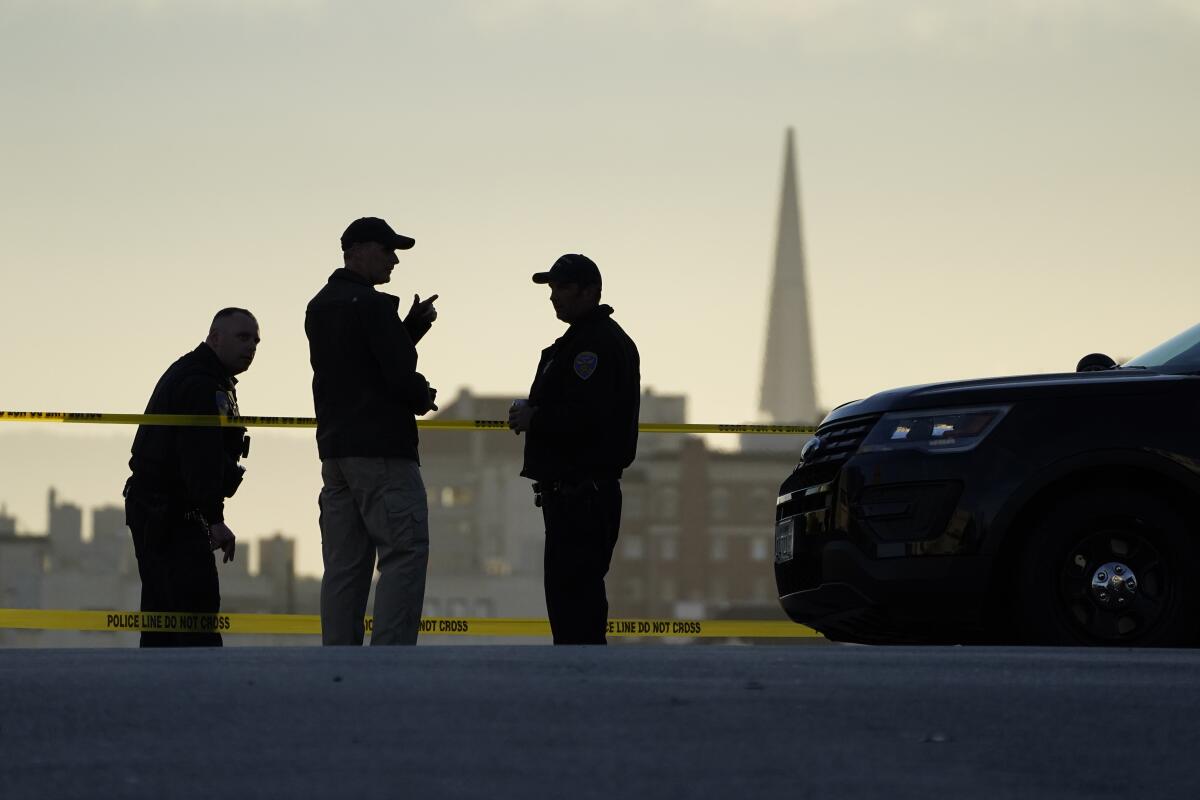 Three police officers stand near a patrol car.