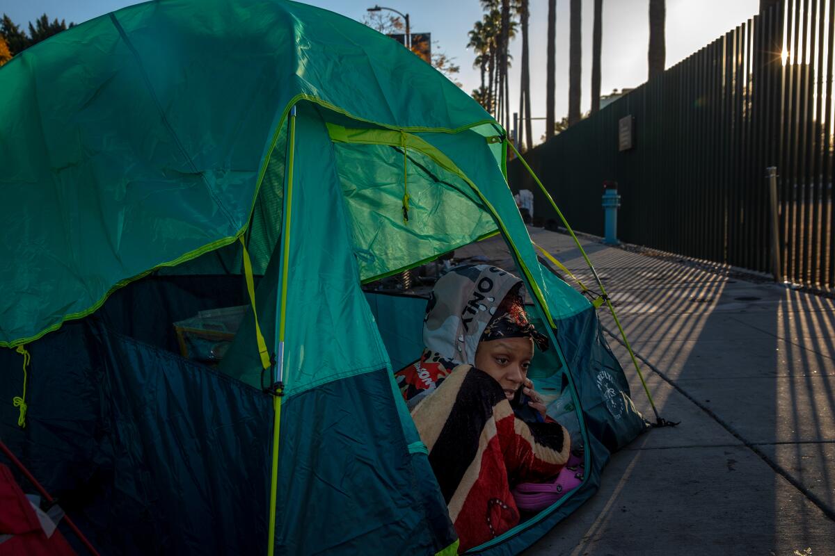 A woman living under tent on a sidewalk next to a fence.