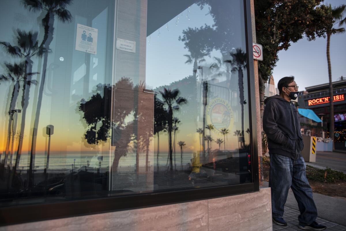 A man wearing a mask walks past a business window with signs about wearing masks