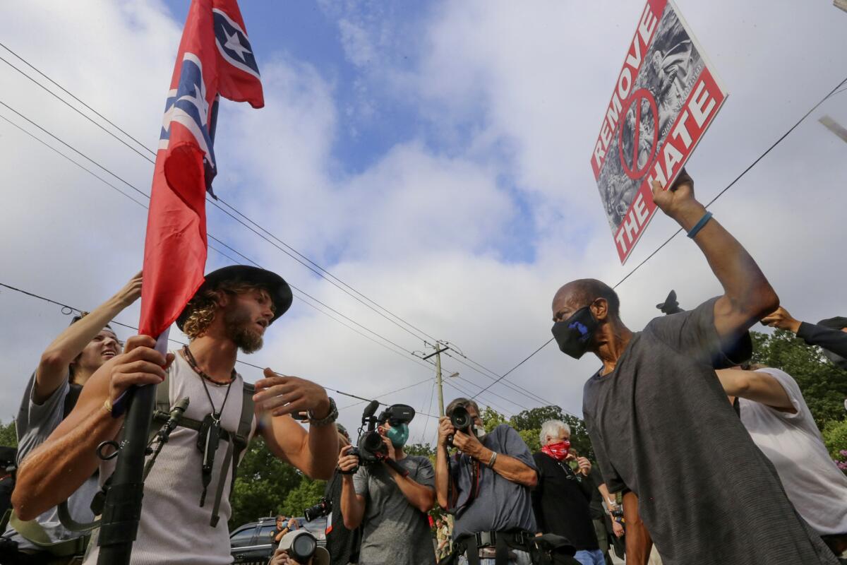 A person with a Confederate flag faces another with a "Remove the Hate" sign
