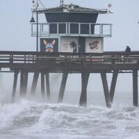 IMPERIAL BEACH, CALIFORNIA - AUGUST 20: People stand on a pier over the Pacific Ocean with Tropical Storm Hilary approaching in San Diego County on August 20, 2023 in Imperial Beach, California. Southern California is under a first-ever tropical storm warning as Hilary approaches with parts of California, Arizona, and Nevada preparing for flooding and heavy rains. All California state beaches have been closed in San Diego and Orange counties in preparation for the impacts from the storm which was downgraded from hurricane status. (Photo by Mario Tama/Getty Images)