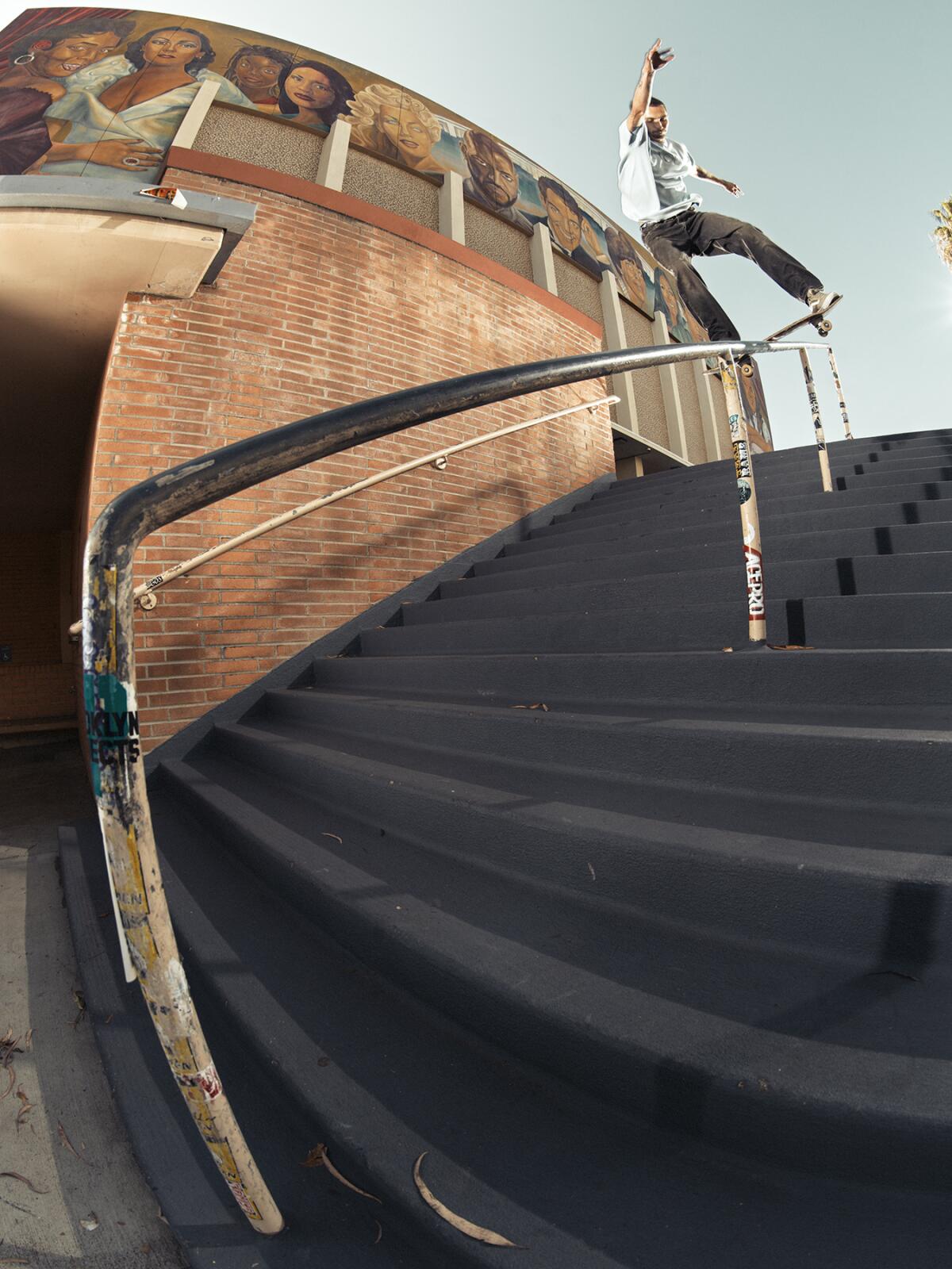 A man on a skateboard rides a handrail on a set of stairs outside a large building.