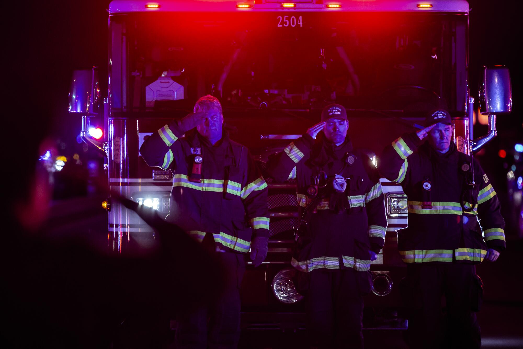 Firefighters salute as a procession carrying the body of a police officer leaves King Sooper's grocery store