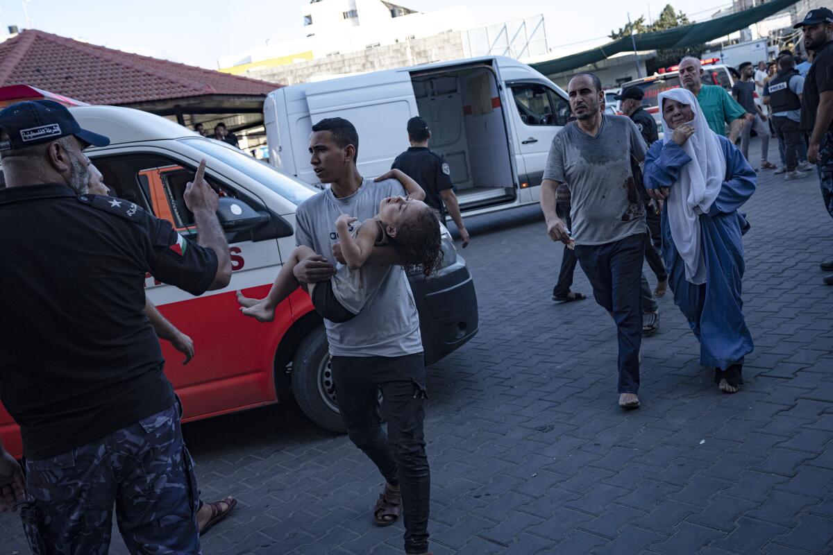 A Palestinian man carries a wounded girl into Shifa Hospital in Gaza City