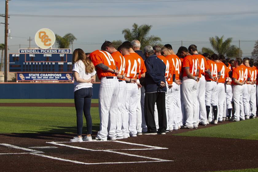 Orange Coast College baseball team bow their heads in silence as they recognize the late OCC baseball coach John Altobelli before Tuesday's game against Southwestern College.