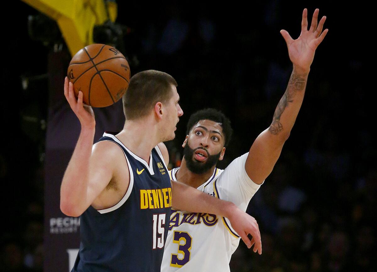 Lakers forward Anthony Davis raises his arm overhead as he defends Nuggets center Nikola Jokic, who looks to make a pass.