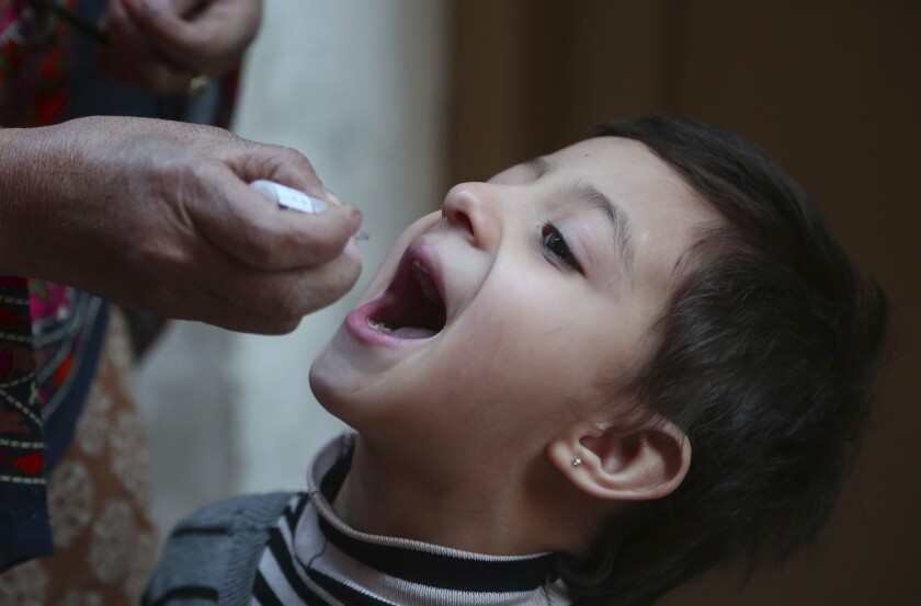 A healthcare worker administers a polio vaccine to a child in Peshawar, Pakistan, Monday, Jan. 11, 2021. Despite a steady rise in coronavirus cases, Pakistan on Monday launched a five-day vaccination campaign against polio amid tight security, hoping to eradicate the crippling children's disease this year. (AP Photo/Muhammad Sajjad)