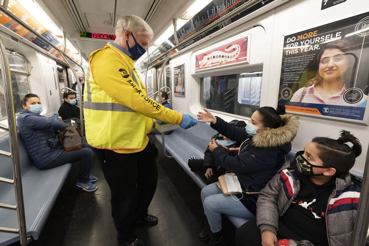 A man in a yellow MTA shirt and vest hands out masks to riders on a New York City subway