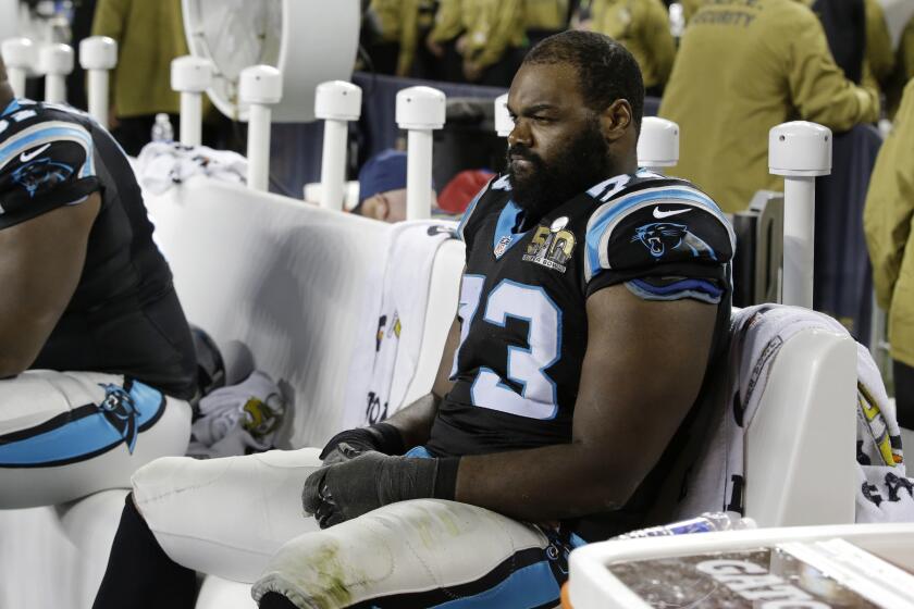 Michael Oher sitting on a bench in a black and light blue football uniform. 