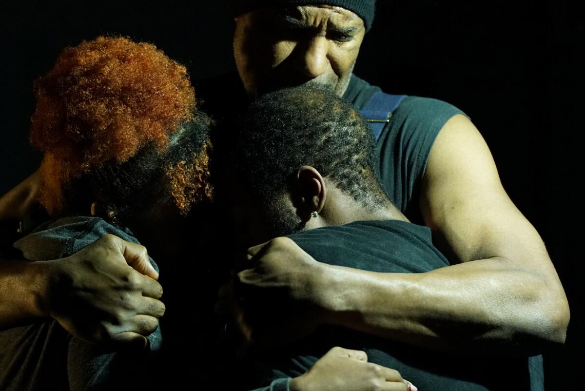 Three dancers in dark clothing embrace in a huddle in a scene from "Sugar Houses"