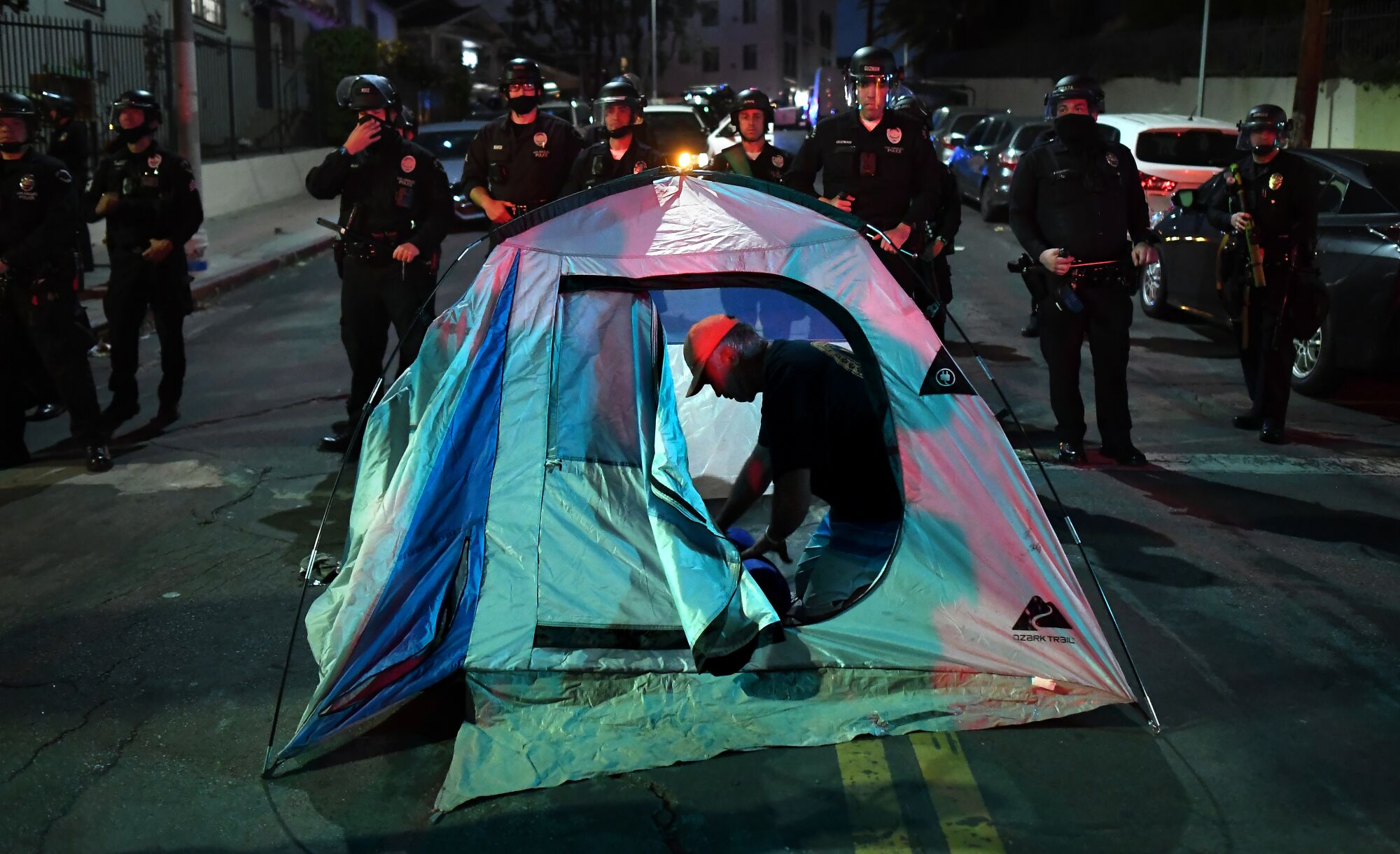 A protestor sets up a tent at Santa Ynez St. and Glendale Ave. as LAPD officers stand guard in Echo Park in March 2021