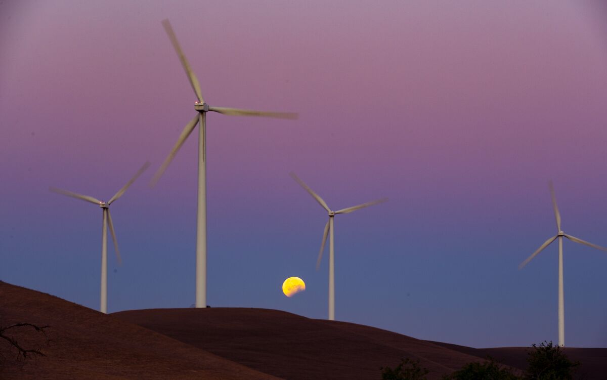 Wind turbines spin with the moon in the background